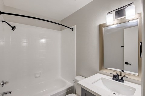 A white bathroom with a white tub, sink, and mirror.