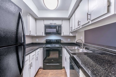 A black fridge in a kitchen with white cabinets.