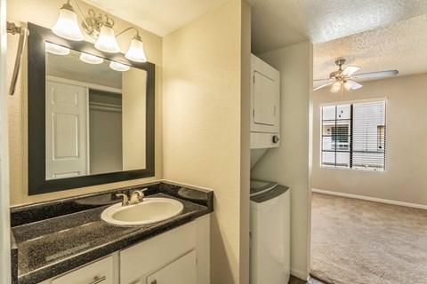 A bathroom with a sink, mirror, and a washer and dryer.