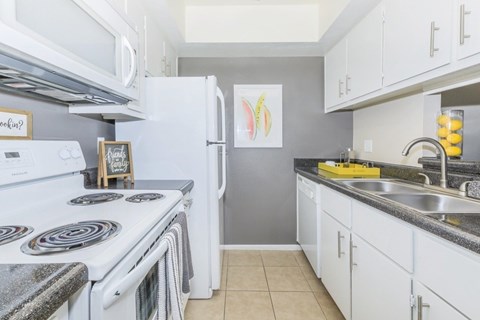 A kitchen with a white stove top oven and white cabinets.