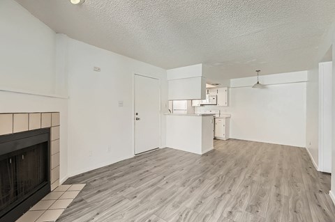 A living room with a fireplace and a kitchen in the background.