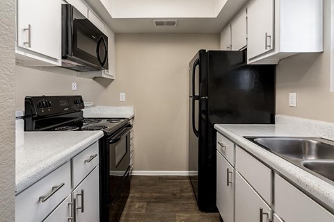 A black refrigerator is in the corner of a kitchen with white cabinets.