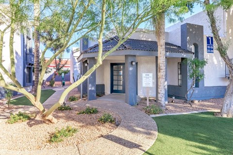 A building with a blue sign on the right side and a tree in front of it.