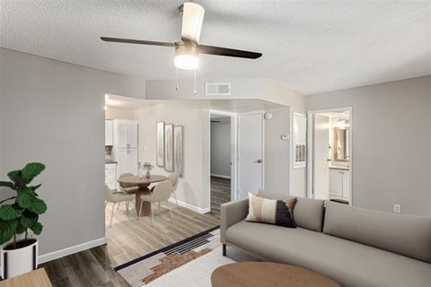 A living room with a couch, a table, a plant, and a ceiling fan.