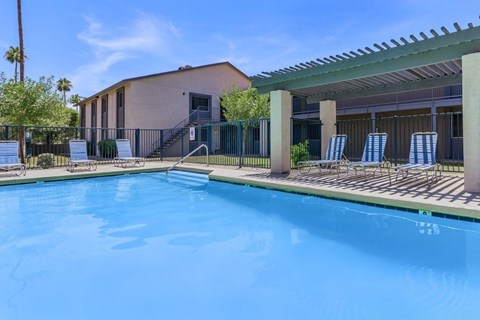 A swimming pool in front of a building with a sunshade over it.