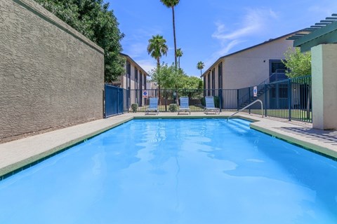 A blue swimming pool surrounded by a fence and a building.