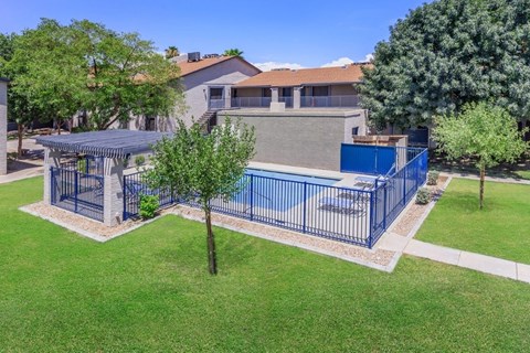 A blue fenced pool surrounded by a grassy area and trees.