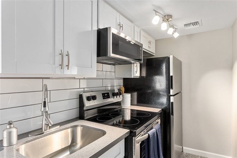 A kitchen with a black refrigerator, stove, and microwave.