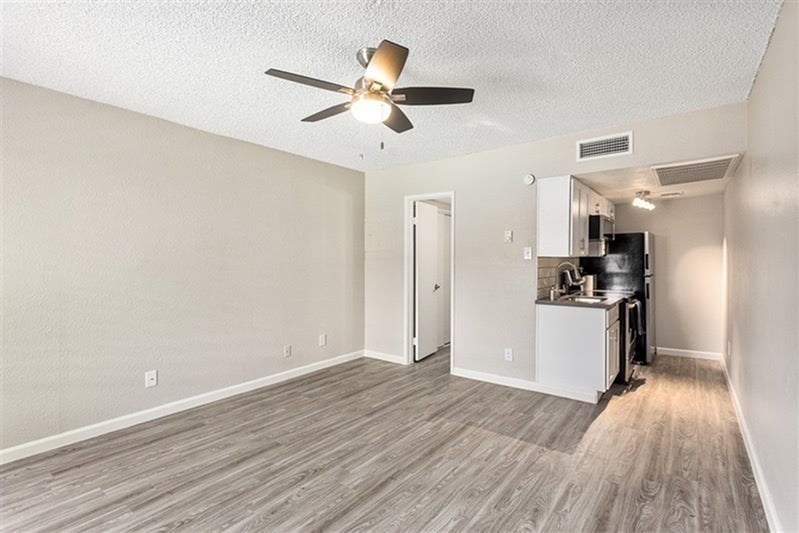 A room with a ceiling fan and a kitchenette in the corner.