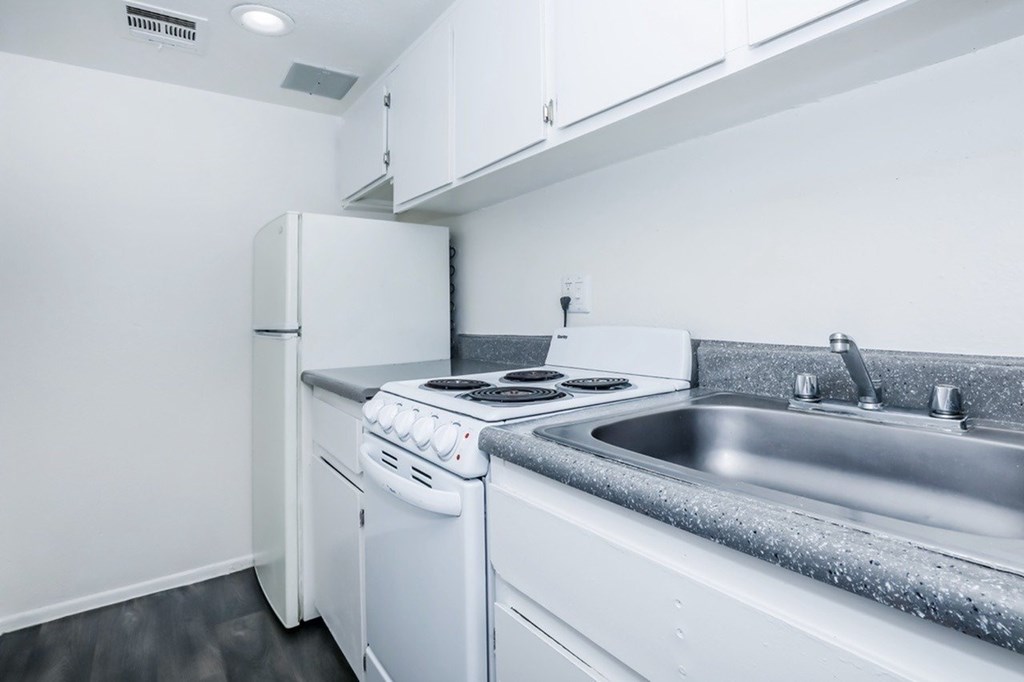 A white kitchen with a stove, sink, and refrigerator.