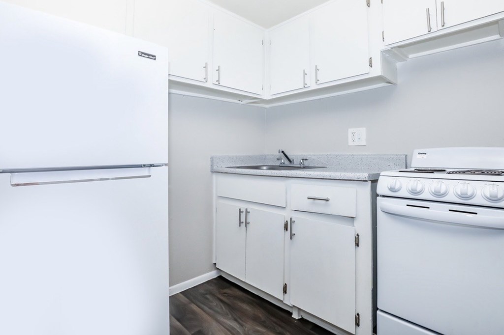 A white refrigerator is in a kitchen with white cabinets and a white stove.
