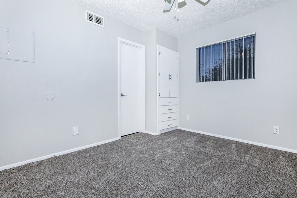 A room with a white door, a white dresser, and a ceiling fan.