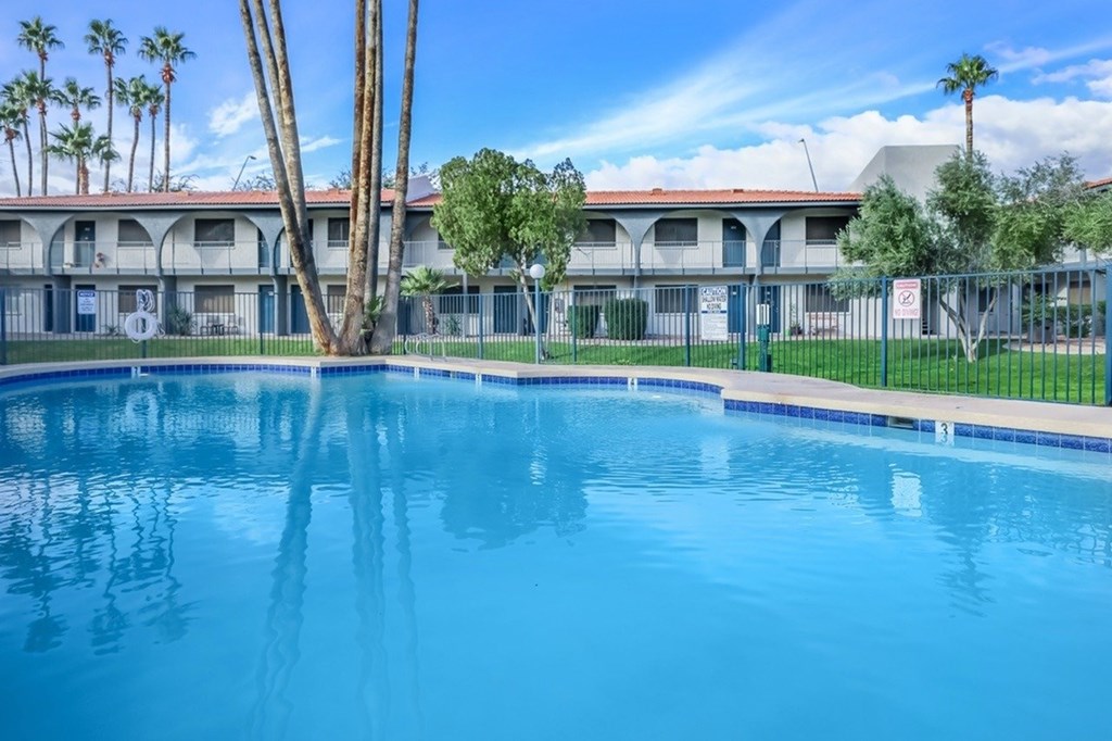 A swimming pool in front of a building with palm trees.