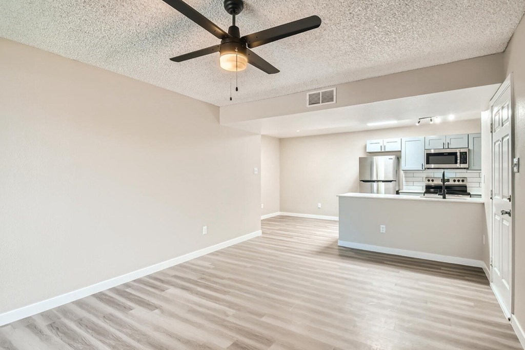 A room with a ceiling fan and a kitchenette in the background.