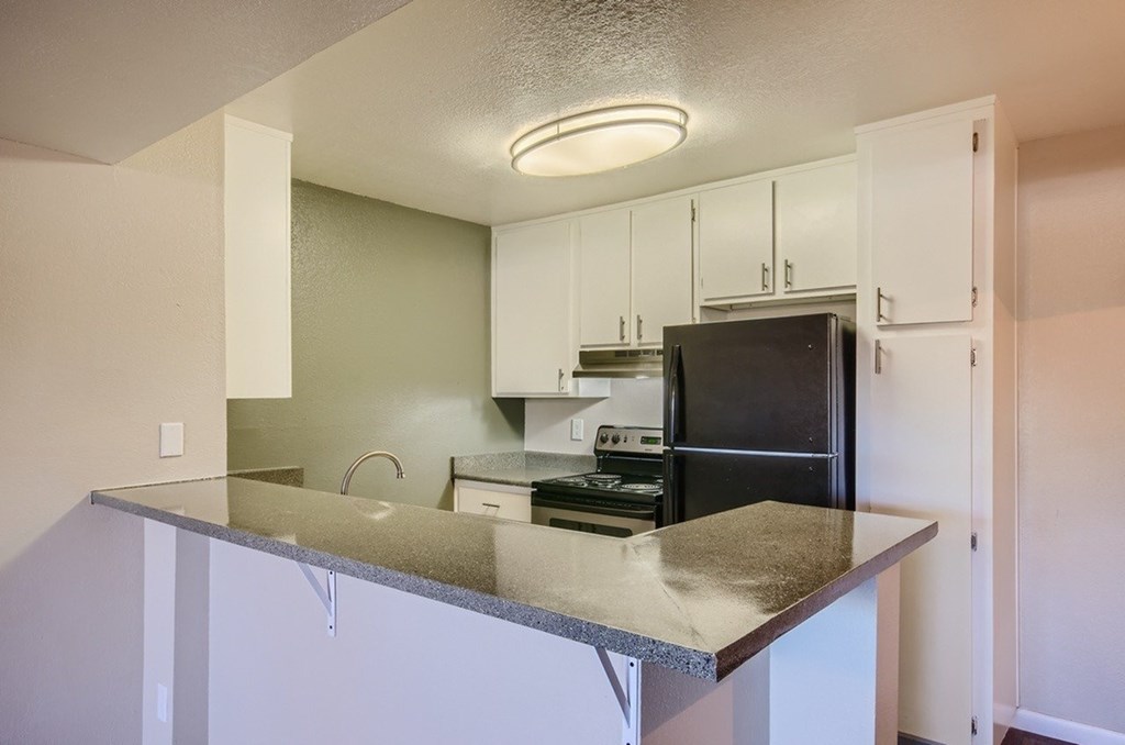 A kitchen with a black refrigerator and white cabinets.
