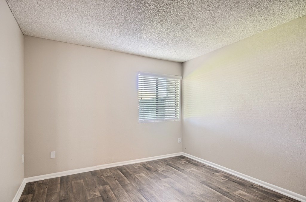 A room with wooden flooring and a window with blinds.