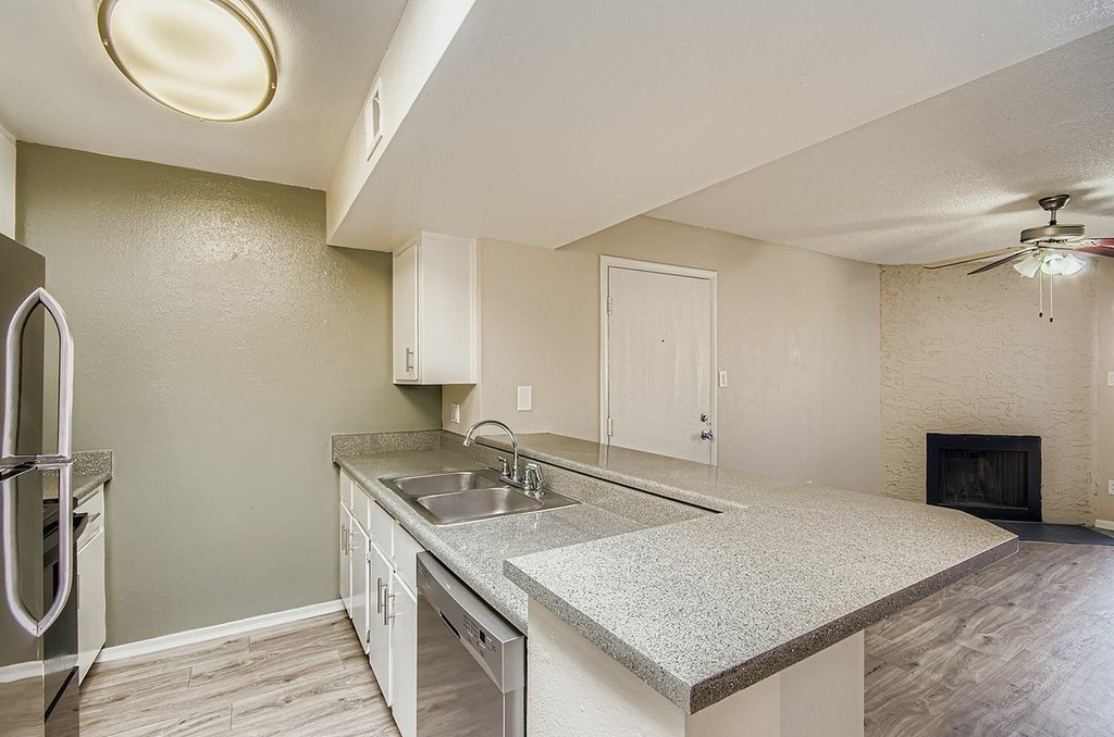 A room with a ceiling fan and a kitchenette in the background.