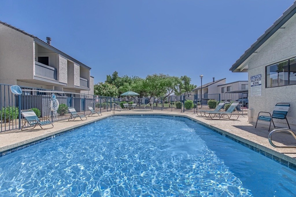 A swimming pool surrounded by chairs and trees.