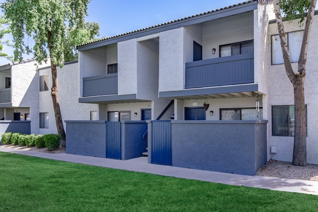 A modern apartment building with a blue fence and a green lawn in front.