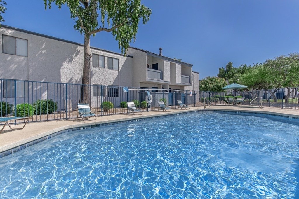 A swimming pool in front of a building with a tree and chairs around it.
