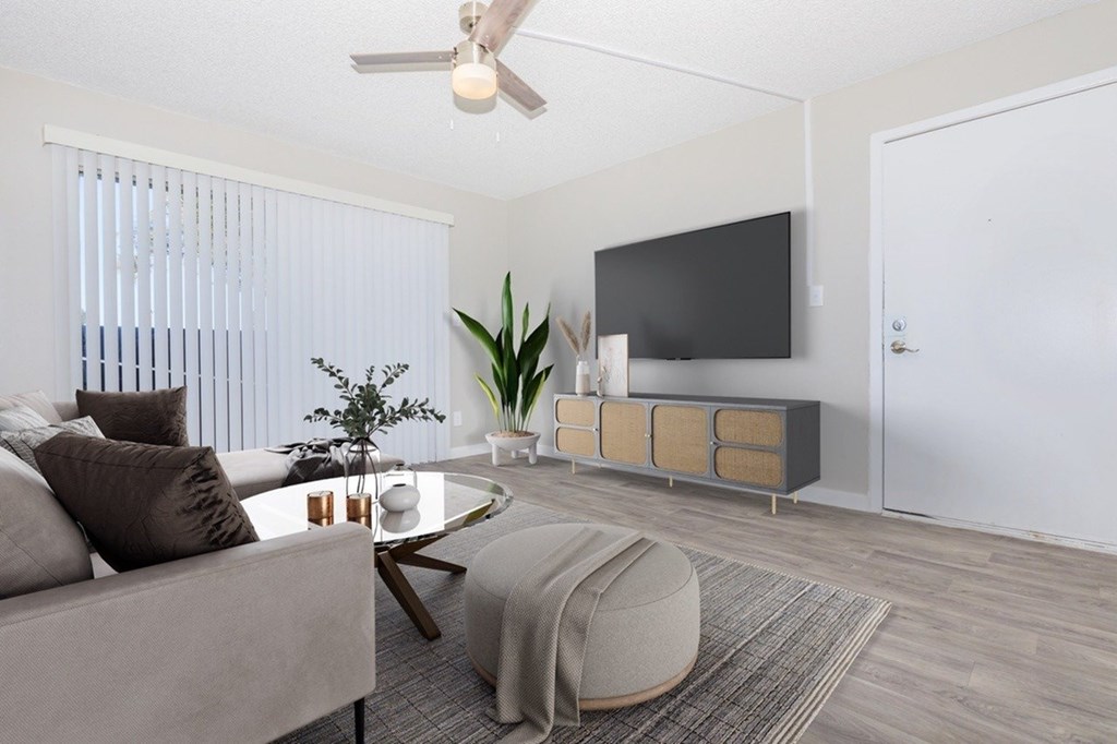 A living room with a grey couch, a coffee table, a ceiling fan, and a television mounted on the wall.