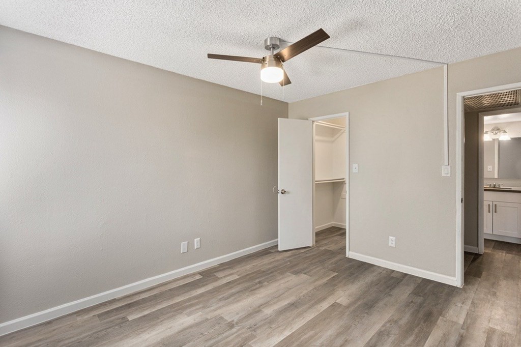 A room with a ceiling fan and light, hardwood floors, and a doorway leading to another room.