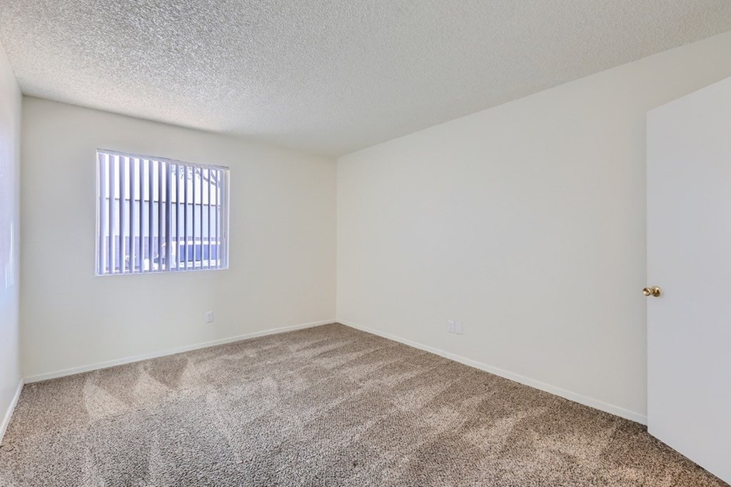 A room with a carpeted floor and a window with blinds.