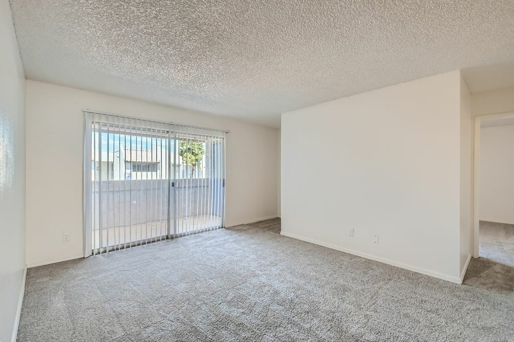A room with a carpeted floor and a window with a view of a building outside.