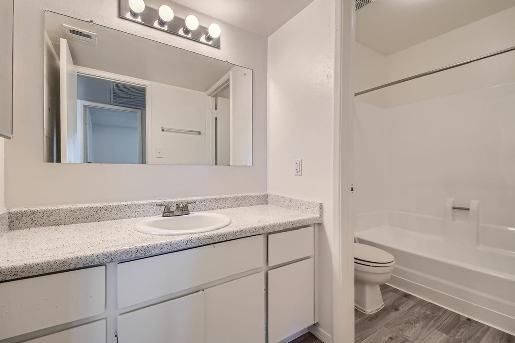 A white bathroom with a sink, mirror, and toilet.