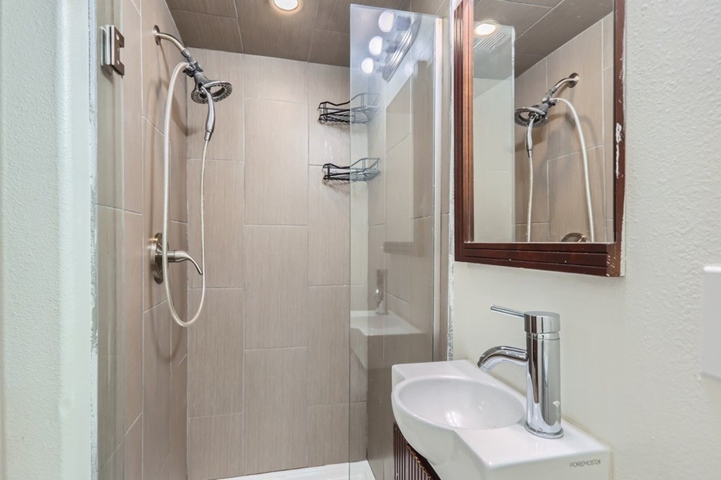 A bathroom with a white sink and a shower with a glass door.