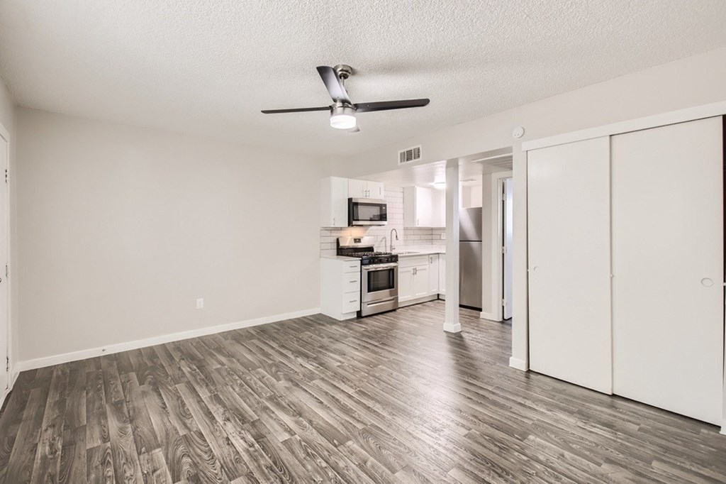 A room with a ceiling fan and a kitchenette in the background.