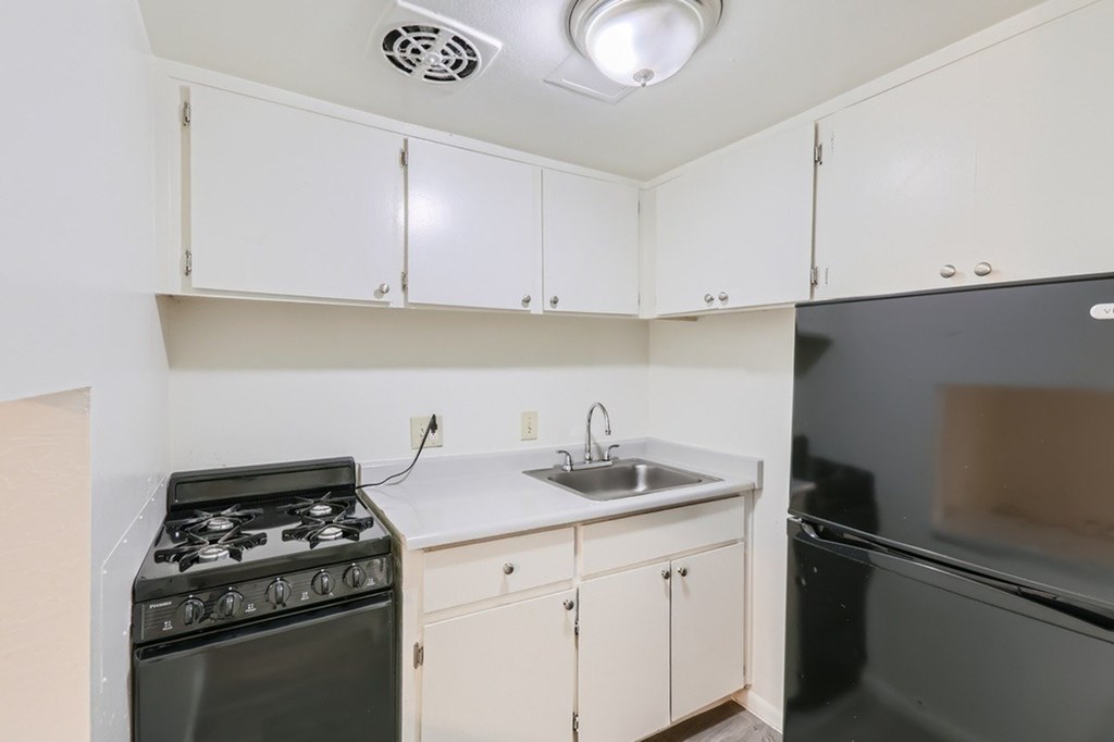 A kitchen with a stove, sink, and cabinets.