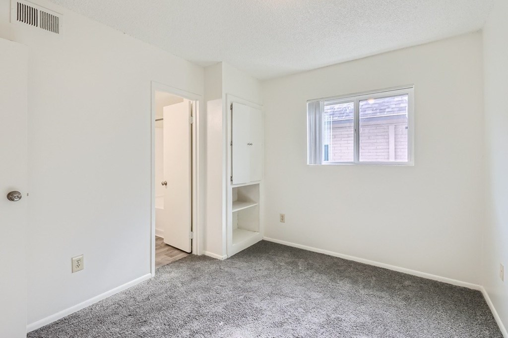 A room with a carpeted floor and a window with blinds.