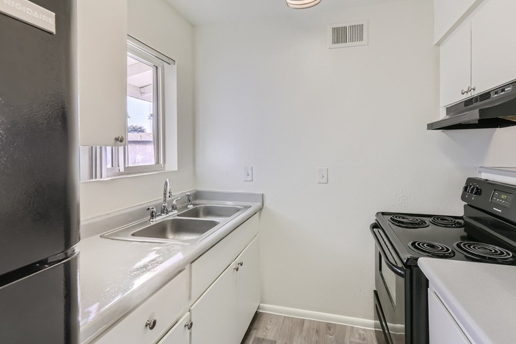A small kitchen with a black fridge, white cabinets, and a stove top oven.