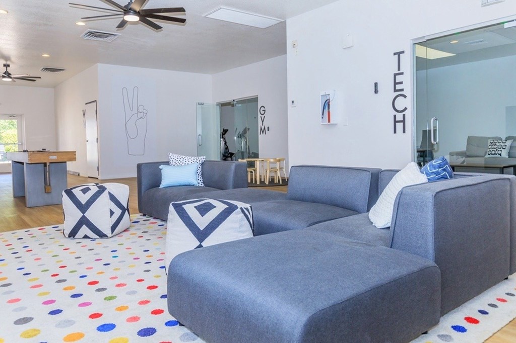 A living room with grey couches and a white wall with the word "TECH" on it.