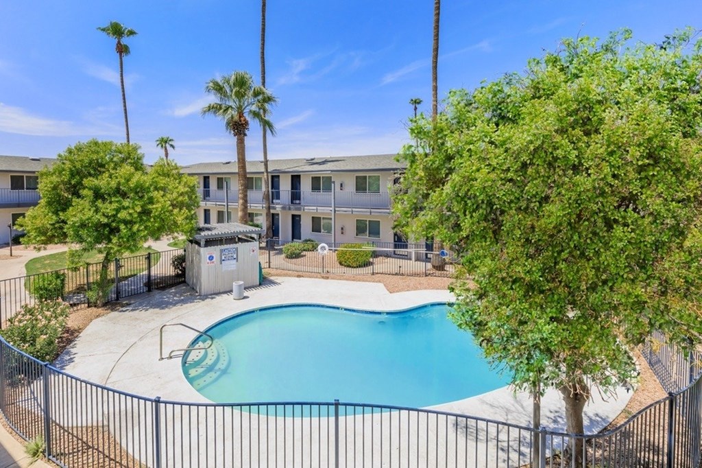 A pool surrounded by a black fence with trees and a building in the background.