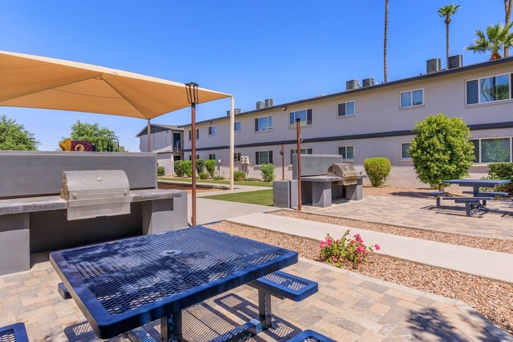 A blue picnic table is in the foreground of a sunny courtyard.