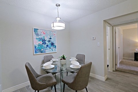 A dining room with a glass table and grey chairs.