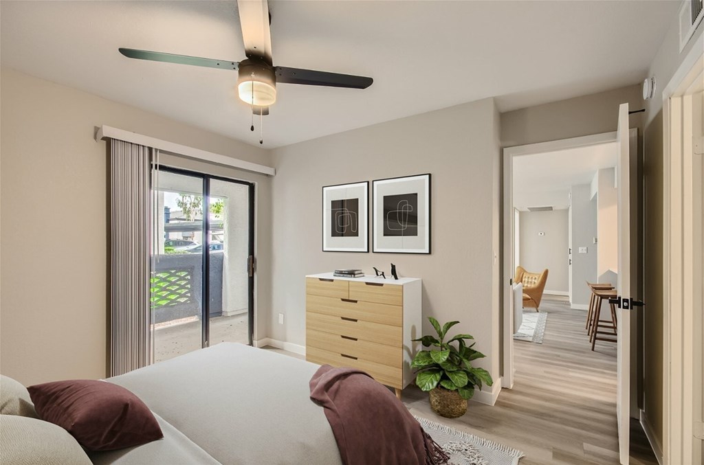 A bedroom with a bed, pillows, a ceiling fan, and a dresser with a mirror above it.