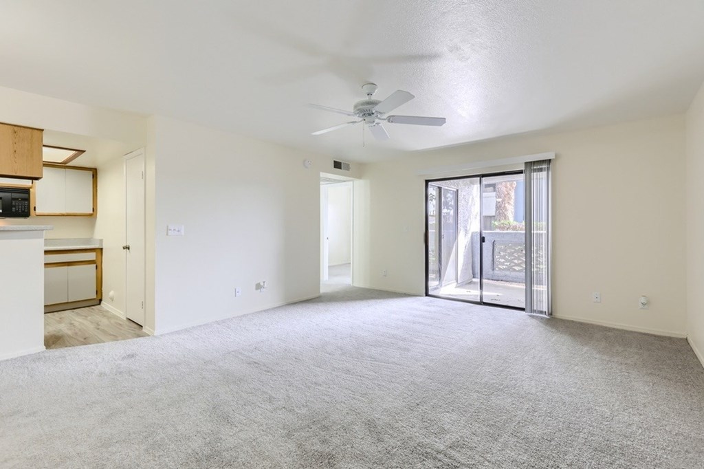 A spacious room with a ceiling fan and sliding glass doors leading to a balcony.