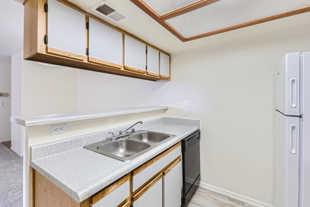 A kitchen with a white fridge, black dishwasher and wooden cabinets.