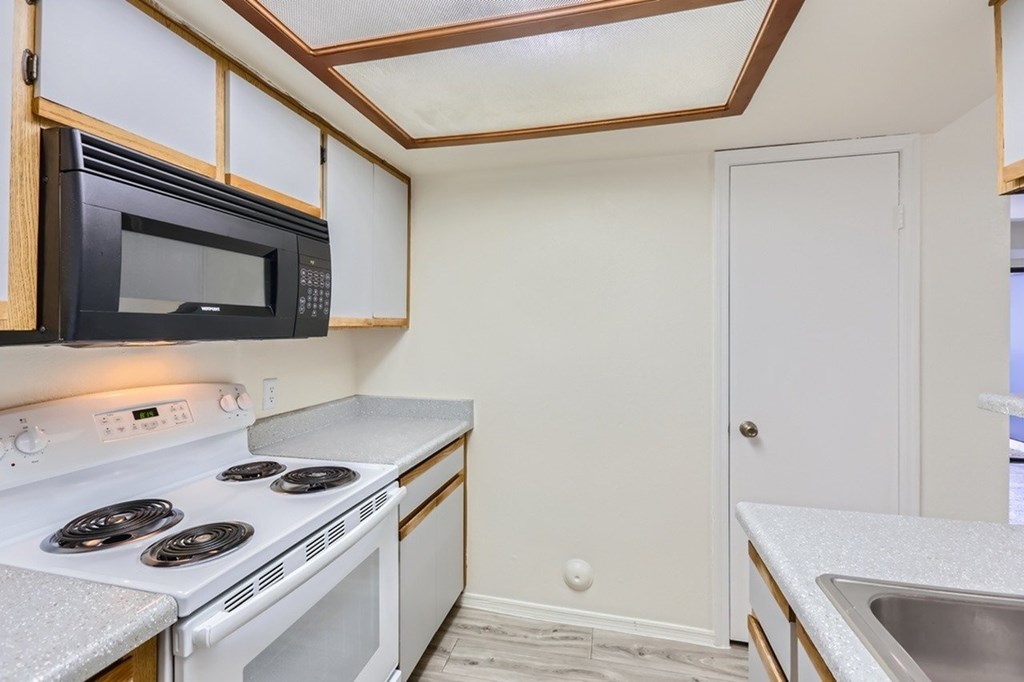 A kitchen with a white stove top oven and a black microwave.