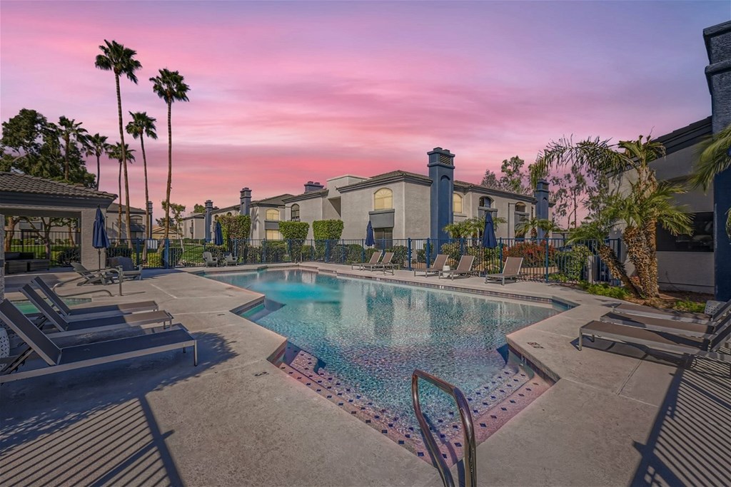 A pool surrounded by lounge chairs and palm trees.
