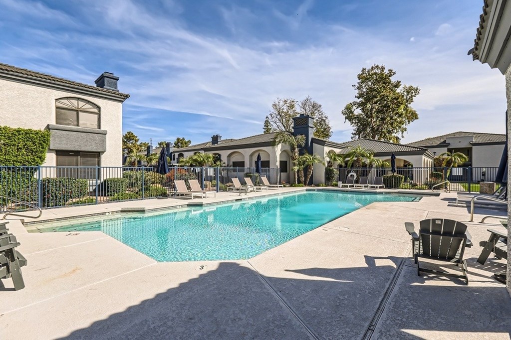 A large swimming pool surrounded by lounge chairs and a building in the background.