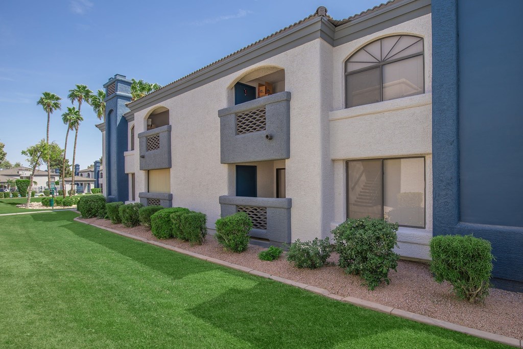 A building with balconies and windows is surrounded by green grass and bushes.