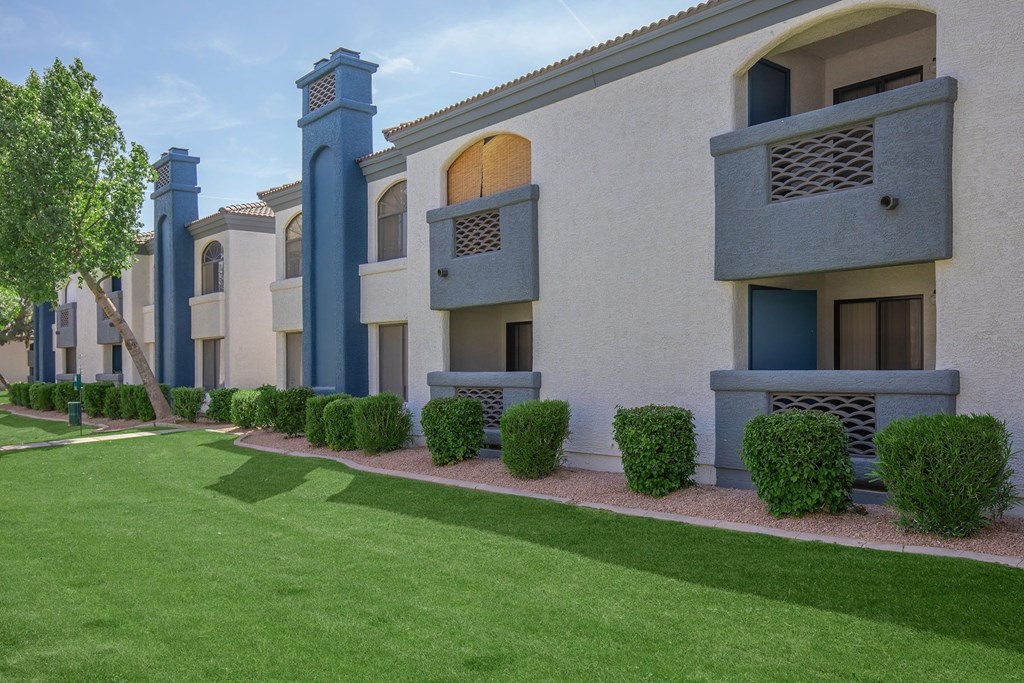 A row of apartment buildings with blue pillars and green bushes in front.