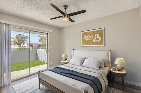 A bedroom with a large bed, a ceiling fan, and a painting on the wall.