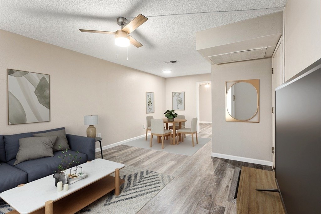 A living room with a grey couch, a coffee table, a dining table with chairs, and a ceiling fan.
