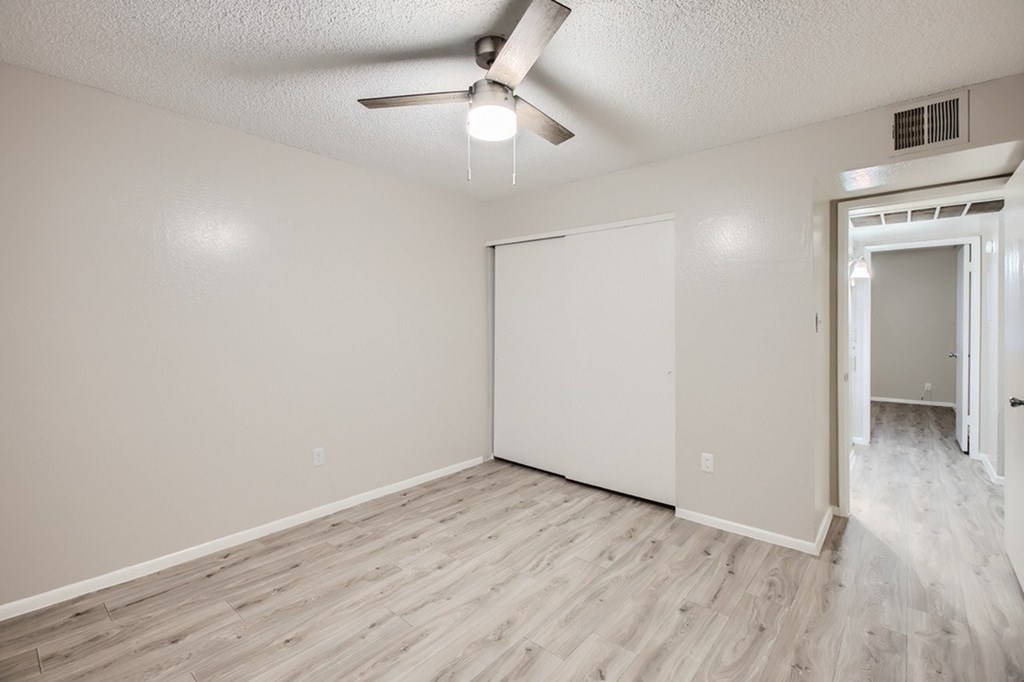 A room with a ceiling fan and light fixture, a door, and a wall with a window.