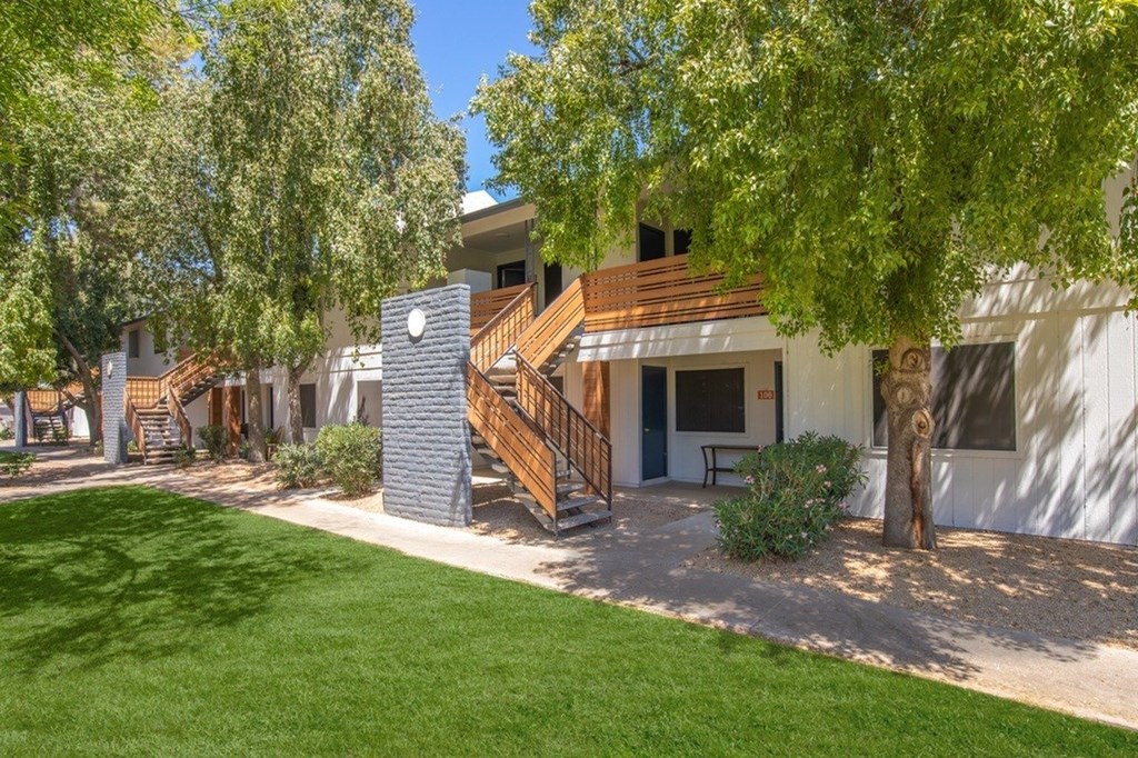 A white house with a brown roof and a tree in front.